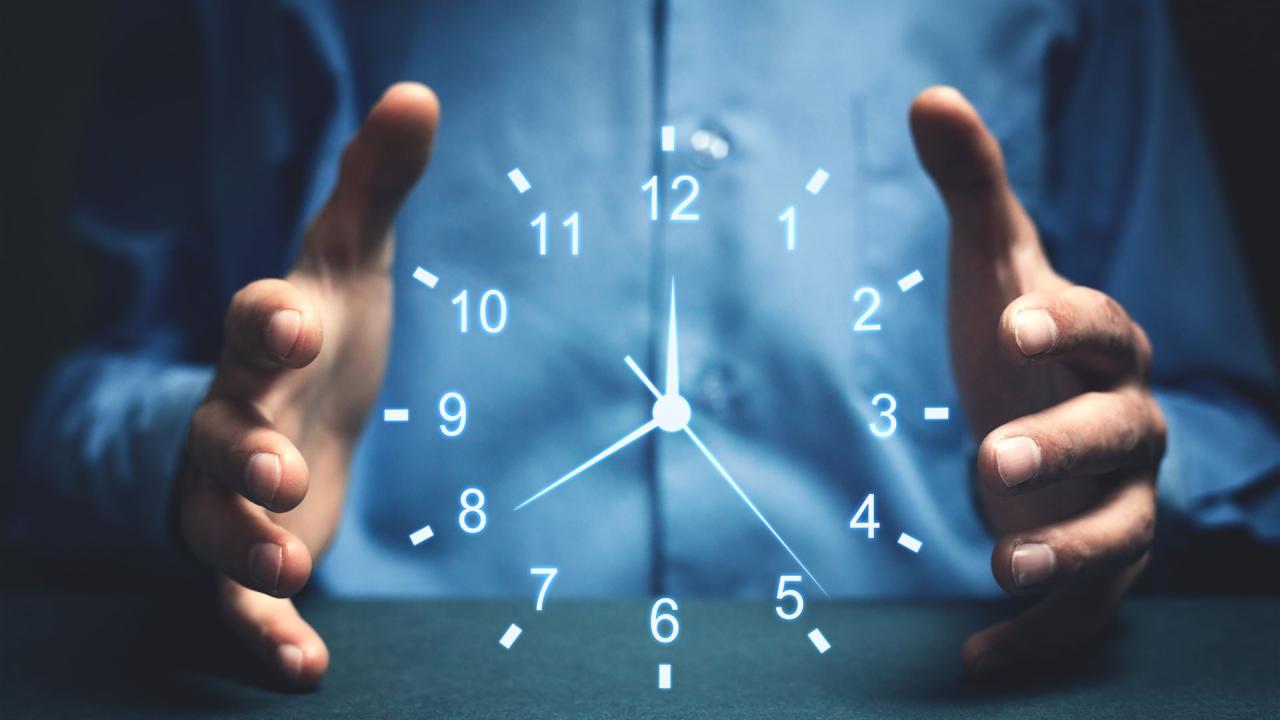 Das Bild zeigt eine Uhr die von einem Mann dahinter mit beiden Händen erfasst wird